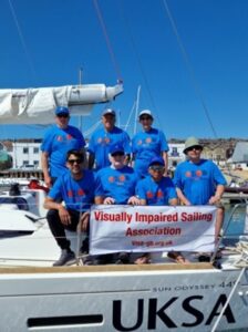 ll seven crew wearing Metro Blind Sport T'shirts, four sitting and three standing behind. They are on the side of the boat looking out, there is the Visa-gb dodger in front and below UKSA is on the side of the boat
