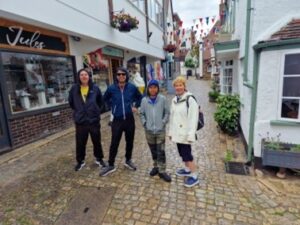 Onshore in Lymington Town, standing on narrow cobbled street, Mihayl, Gareth, Ollie and Helen are facing the camera, there is some bunting strung between the buildings.