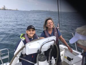 Visually Impaired sailor Vjay  is at the wheel, yacht skipper Rosie to his left with a broad smile. to his left. 